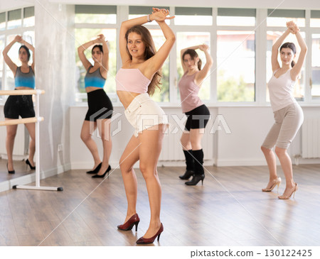 Women wearing casual activewear performing sensual and modern high heels choreography during group class in studio Women wearing casual activewear performing sensual and modern high heels choreography during group class in studio 130122425