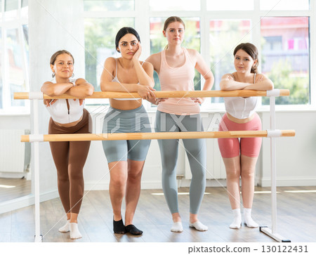 Young female ballet students relaxing at barre in studio 130122431