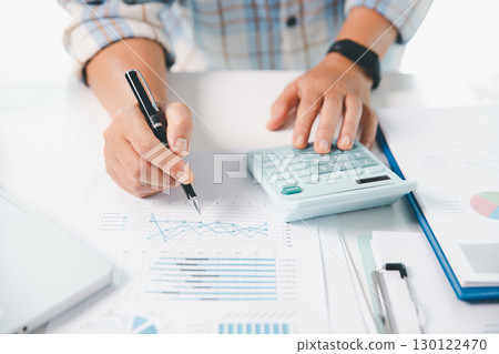 Accountant working on desk using calculator for calculate finance report in office. business finance, calculate tax by organizing financial documents, tracking income investment, accounting by hand. 130122470