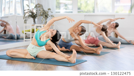 Women exercising Hatha yoga in fitness studio, sitting on mat and doing stretching in Parivrtta Janu Sirsasana 130122475