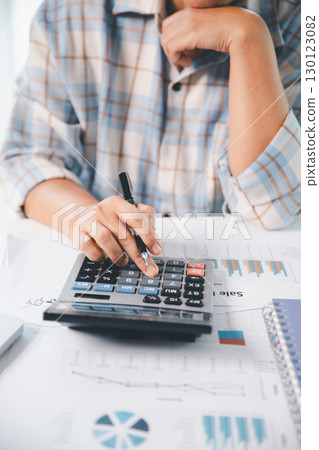 Accountant working on desk using calculator for calculate finance report in office. business finance, calculate tax by organizing financial documents, tracking income investment, accounting by hand. 130123082