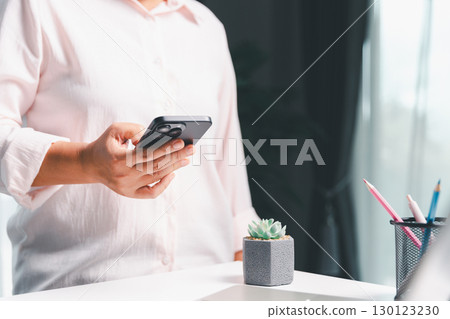 Close-up shot, woman sits at a wooden table using her smartphone, with her finger touching the phone screen as she navigates mobile banking, online shopping, and social media networks. Close-up shot, woman sits at a wooden table using her smartphone, with her finger touching the phone screen as she navigates mobile banking, online shopping, and social media networks. 130123230