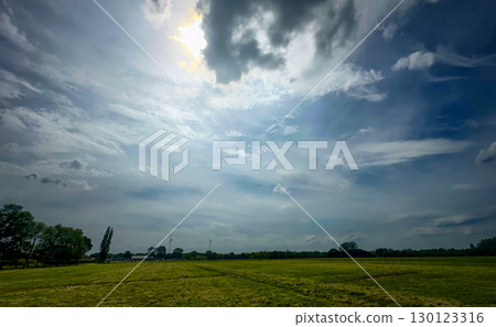 Expansive Landscape Featuring a Dramatic Sky Above Vibrant and Lush Green Fields Expansive Landscape Featuring a Dramatic Sky Above Vibrant and Lush Green Fields 130123316