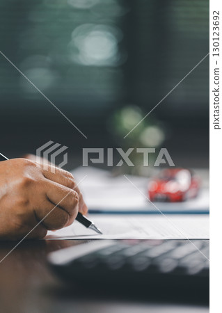 Client is signing the contract and insurance document for the purchase of a vehicle, finalizing finance and loan agreements that mark the approval of a smart investment and successful car deal. Client is signing the contract and insurance document for the purchase of a vehicle, finalizing finance and loan agreements that mark the approval of a smart investment and successful car deal. 130123692