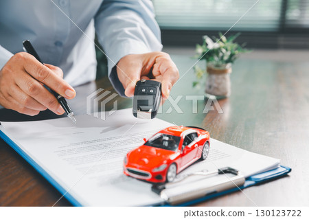 Businesswoman signing car insurance document or lease paper. Writing signature on contract or agreement. Buying or selling new or used vehicle. Car keys on table. Warranty or guarantee. Businesswoman signing car insurance document or lease paper. Writing signature on contract or agreement. Buying or selling new or used vehicle. Car keys on table. Warranty or guarantee. 130123722