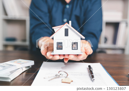 Model house, stacks of coins, calculator, financial documents on a wooden desk represent real estate investment and mortgage planning, highlighting financial growth and strategic planning strategies. 130123807