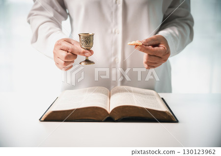 During the holy communion ceremony in church, a hand is extended in faith to receive the sacred sacrament, reflecting the spiritual and religious worship central to Christianity. 130123962