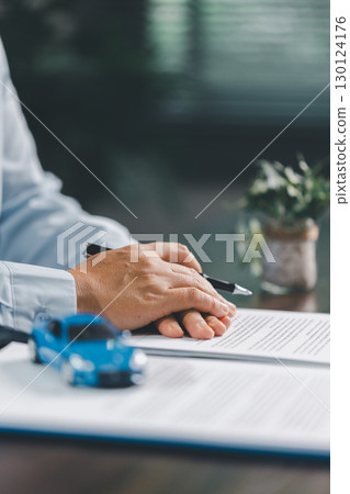 Business office, woman employee finalizes deal with client, handing over car key after signing contract and reviewing insurance and loan documents for sale or rent of vehicle at table. Business office, woman employee finalizes deal with client, handing over car key after signing contract and reviewing insurance and loan documents for sale or rent of vehicle at table. 130124176