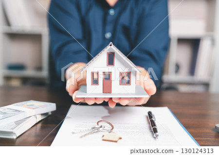 Model house, stacks of coins, calculator, financial documents on a wooden desk represent real estate investment and mortgage planning, highlighting financial growth and strategic planning strategies. 130124313