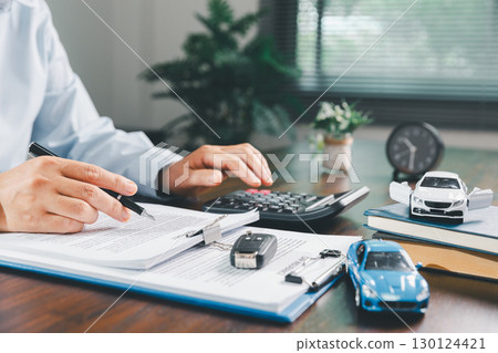 Businesswoman signing car insurance document or lease paper. Writing signature on contract or agreement. Buying or selling new or used vehicle. Car keys on table. Warranty or guarantee. 130124421