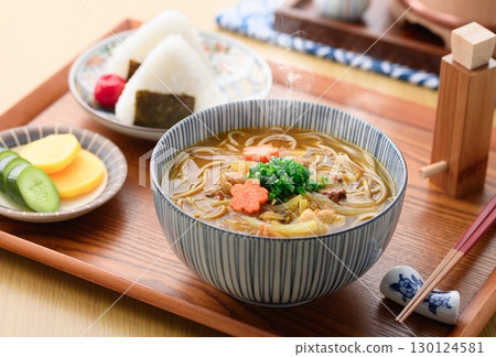 熱咖哩蕎麥麵和飯糰套餐的日式美食場景。圖片中是桌上熱氣騰騰的麵條和醃菜。 130124581