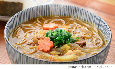 Japanese food scene of hot curry soba and rice ball set meal. Image of steaming noodle dish and pickles on the table. Japanese food scene of hot curry soba and rice ball set meal. Image of steaming noodle dish and pickles on the table. 130124582