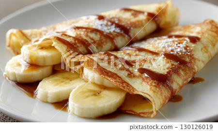 Banana crepe with syrup and powdered sugar on white plate, delicious breakfast or dessert with fresh fruit and sweet topping 130126019