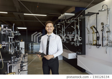Portrait of a smiling young man selling faucets in a plumbing shop. Portrait of a smiling young man selling faucets in a plumbing shop. 130126134