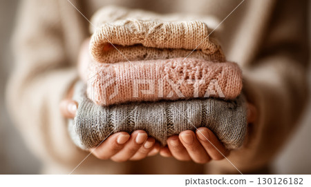 Soft knitted sweater stack held in hands with warm beige, pink, and gray colors creating cozy and comforting feeling in image 130126182