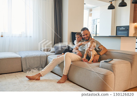 Smiling, positive facial expression. Father with two baby boys is sitting at sofa 130126820