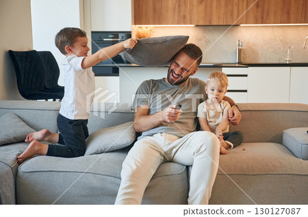 Pillow push by the kid. Father with two baby boys is sitting at sofa 130127087