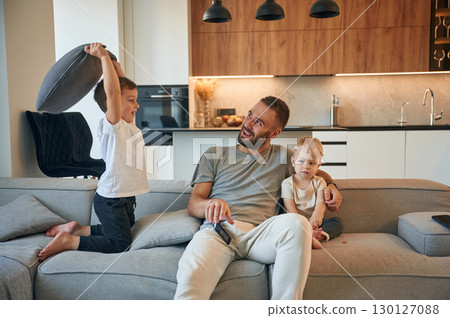 Pillow push by the kid. Father with two baby boys is sitting at sofa 130127088