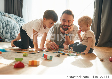 Lying down, board game. Father is playing with two little boys on the floor with toys Lying down, board game. Father is playing with two little boys on the floor with toys 130127111