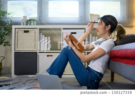Young woman in casual outfit reflecting and writing in notebook Young woman in casual outfit reflecting and writing in notebook 130127339