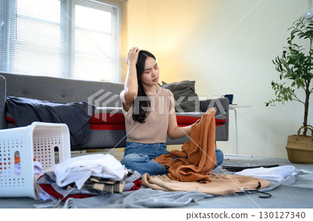 Tired female organizing messy laundry pile with frustrated expression Tired female organizing messy laundry pile with frustrated expression 130127340