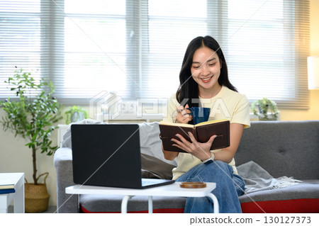 Smiling woman holding notebook and coffee cup while working from home. Smiling woman holding notebook and coffee cup while working from home. 130127373