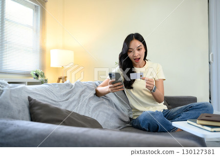 Excited woman holding credit card and smartphone, surprised by online shopping deal Excited woman holding credit card and smartphone, surprised by online shopping deal 130127381