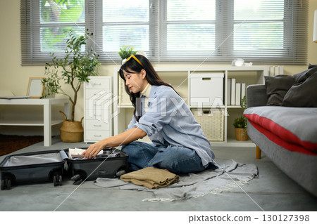 Female traveler organizing her luggage at home before a trip, folding clothes neatly 130127398