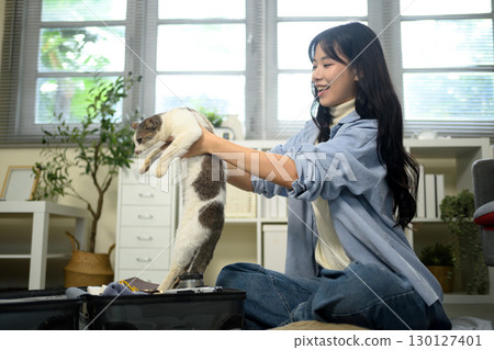 Young woman lifting her cat while packing a suitcase and preparing for travel at home 130127401