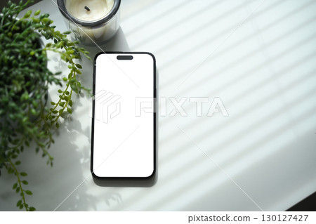 Smartphone with blank screen mockup placed on white desk with plant and candle Smartphone with blank screen mockup placed on white desk with plant and candle 130127427