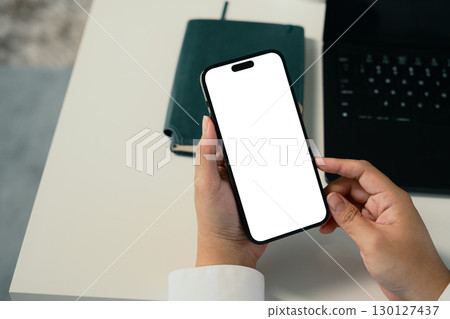 Close up of a person holding smartphone with blank white screen sitting at workplace Close up of a person holding smartphone with blank white screen sitting at workplace 130127437
