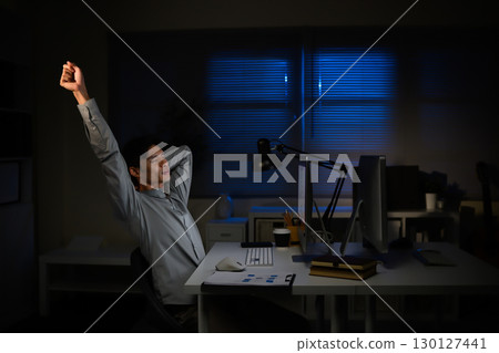 Overworked worker taking a break from computer tasks, stretching after long hours of screen time 130127441