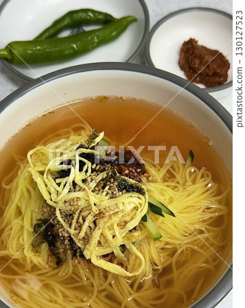Janchi Guksu, a light and savory Korean noodle dish served in a clear broth, topped with vegetables, egg strips, and seaweed. A simple yet flavorful meal often enjoyed on special occasions. 130127523