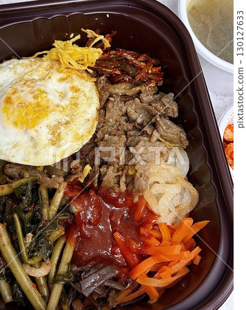 Bibimbap, a vibrant Korean rice dish topped with a variety of seasoned vegetables, gochujang, and a fried egg, often accompanied by sliced meat. Mixed together, it creates a flavorful and balanced. 130127633