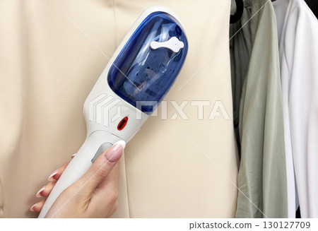 Woman ironing clothes with steam iron at wardrobe. Clothes care and garment steaming. Fashion, laundry, household chores, wrinkle removal. Business and casual clothing care 130127709