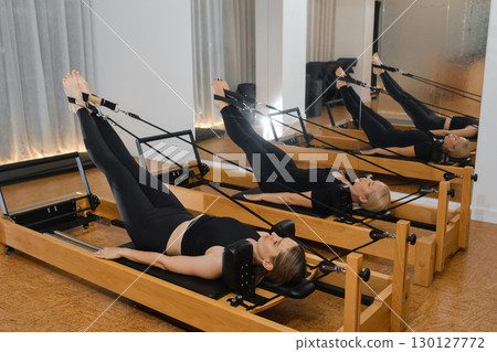 Pilates workout session featuring multiple individuals using reformer machines in a modern studio during afternoon hours Pilates workout session featuring multiple individuals using reformer machines in a modern studio during afternoon hours 130127772