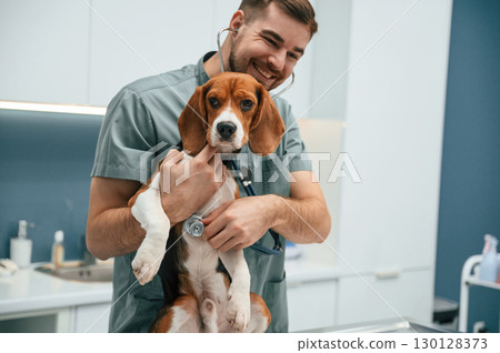 Positive man is holding animal. Dog in veterinarian clinic with male doctor Positive man is holding animal. Dog in veterinarian clinic with male doctor 130128373