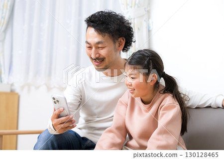 父親和女兒在家裡的沙發上一起看智慧型手機 130128465