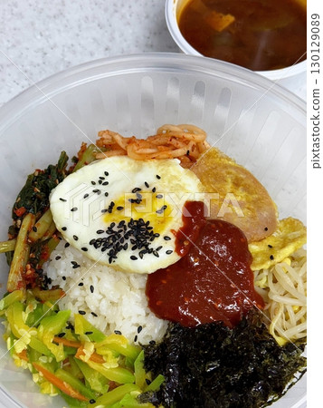 Bibimbap, a vibrant Korean rice dish topped with a variety of seasoned vegetables, gochujang, and a fried egg, often accompanied by sliced meat. Mixed together, it creates a flavorful and balanced. 130129089