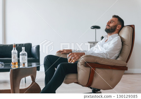 Glass of whiskey in hand. Upset young man drinker alcoholic is indoors 130129385