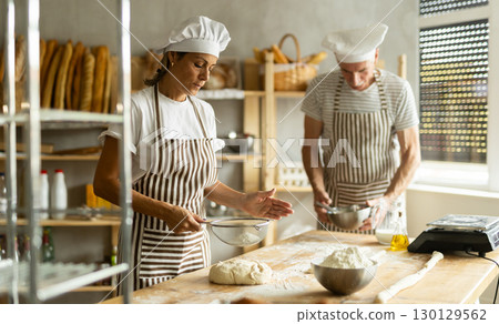 Elderly man and woman sift flour and whipping dough 130129562