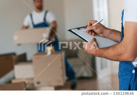 Document in hands. Two moving service employees in a room Document in hands. Two moving service employees in a room 130129636