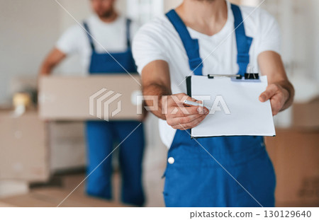 Close up view. Holding blank document to sign. Two moving service employees in a room Close up view. Holding blank document to sign. Two moving service employees in a room 130129640