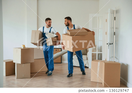 Boxes in hands. Two moving service employees in a room Boxes in hands. Two moving service employees in a room 130129747