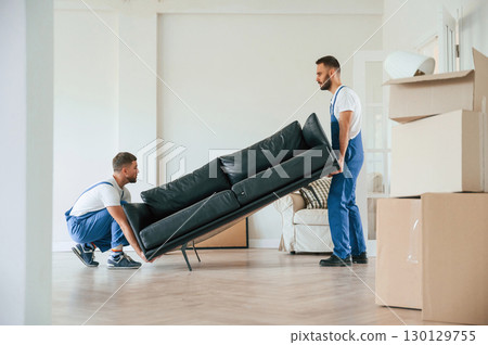 Holding heavy sofa. Two moving service employees in a room 130129755