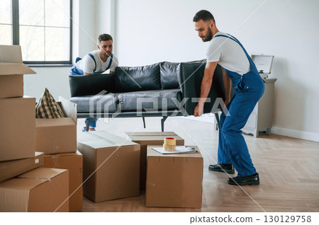 Holding heavy sofa. Two moving service employees in a room 130129758