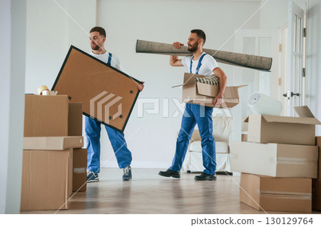 Painting and mat in hands. Two moving service employees in a room 130129764