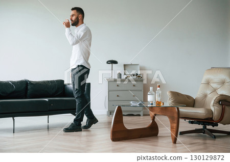 Walking and drinking whiskey. Upset young man alcoholic is indoors 130129872