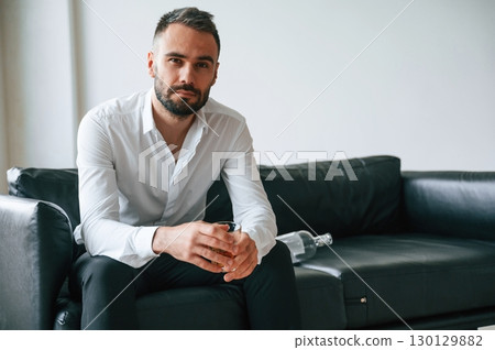 Sitting on he sofa. Upset young man drinker alcoholic is indoors Sitting on he sofa. Upset young man drinker alcoholic is indoors 130129882