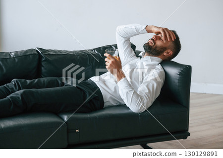 Having headache, lying down on the sofa. Upset young man drinker alcoholic is indoors Having headache, lying down on the sofa. Upset young man drinker alcoholic is indoors 130129891